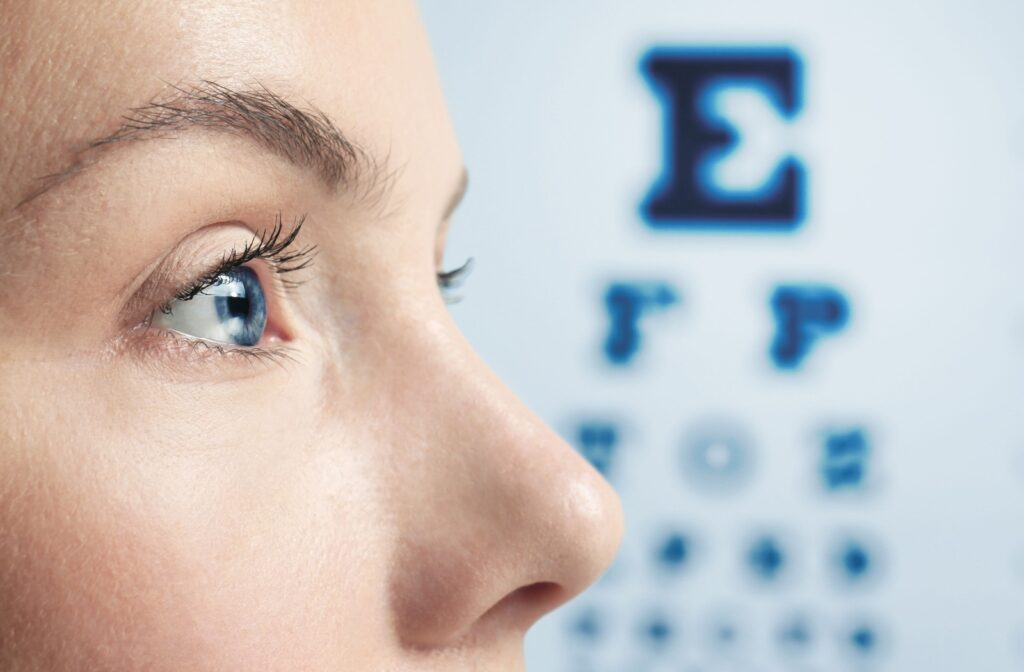A closeup of a woman's eye at the eye doctor with a visual acuity chart in the background.