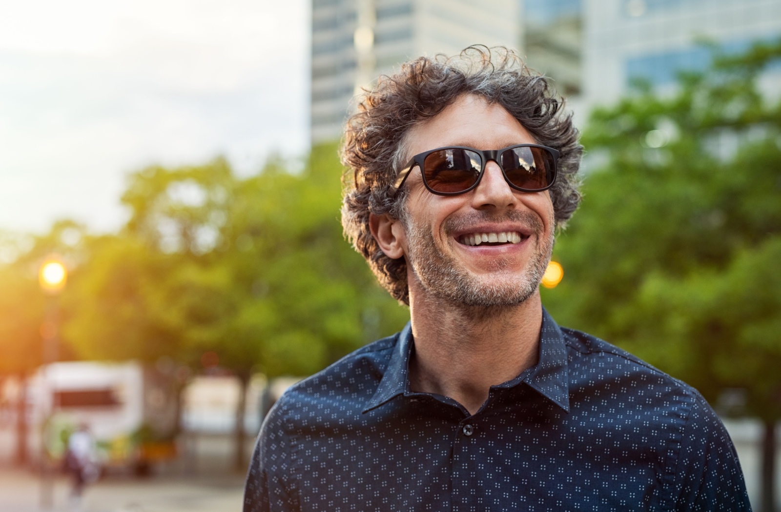 A smiling person protects their eyes with stylish sunglasses on a sunny day.