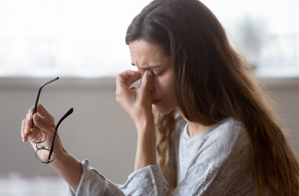 A woman rubbing her eyes while holding glasses, possibly experiencing discomfort from wearing incorrect prescription lenses.