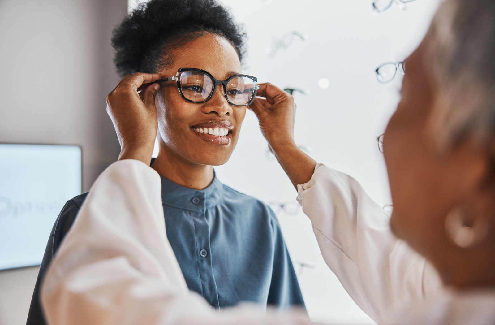 Optician fitting glasses on a smiling woman during an eye exam.