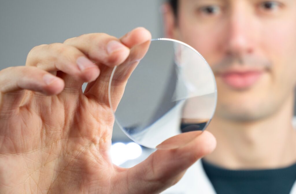 A close-up image of an eye doctor holding a glasses lens in their right hand.