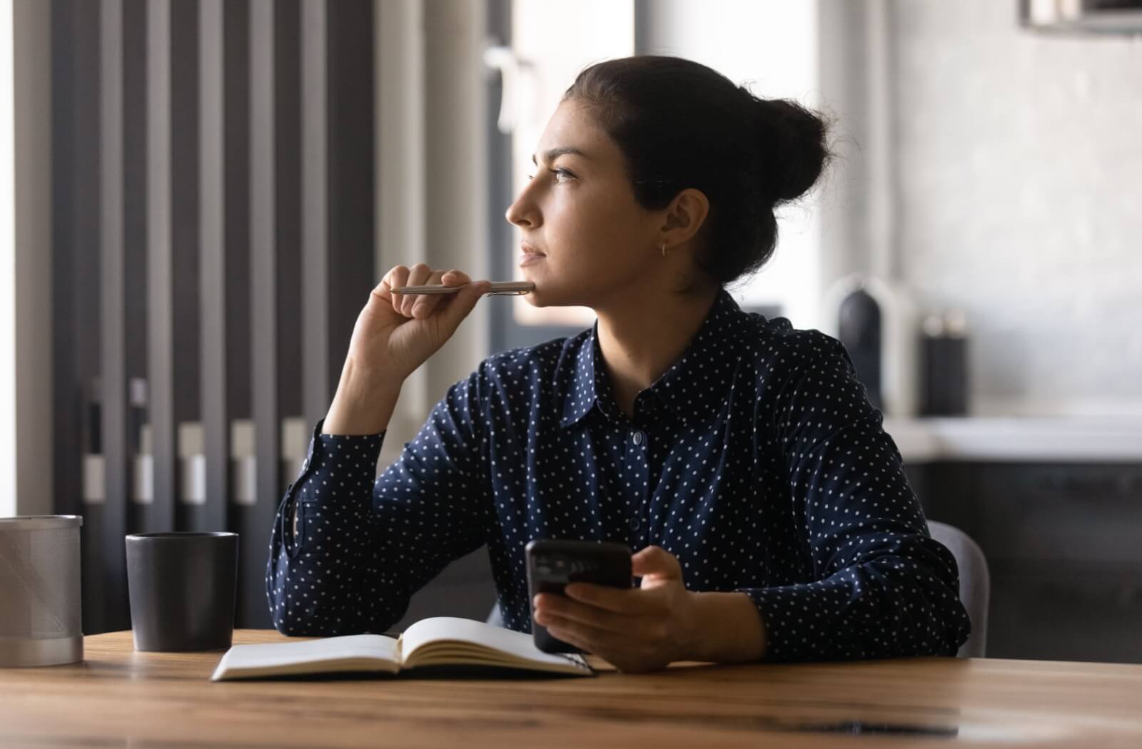 A person holds a smartphone and pen while looking out a window to give their eyes a break.