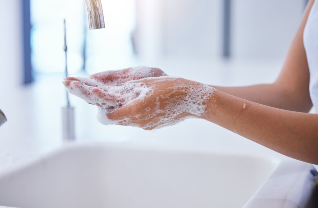 A person washes their hands under a faucet with soap and lathered bubbles.