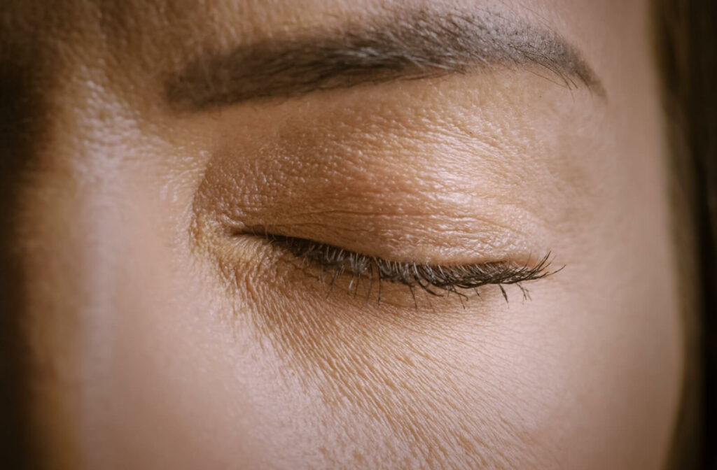 An extreme close-up of a person's closed eye and eyelid, highlighting the skin texture and eyelashes.